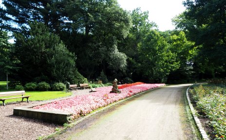 Ein Weg durch den Schlosspark in Sebaldsbrück. Links vom Weg ist ein großes Blumenbeet mit einer Statue, dahinter sind Bänke